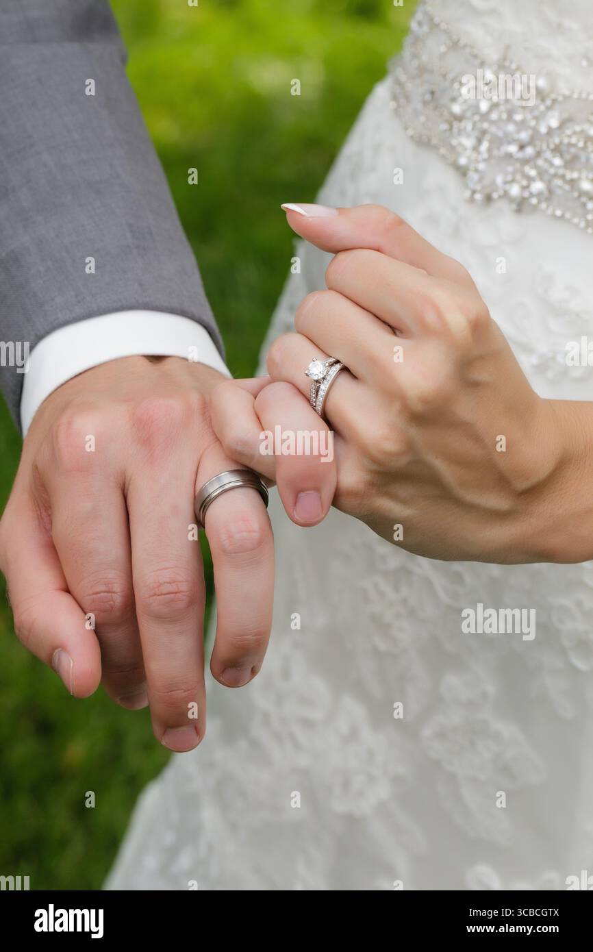 La sposa e lo sposo si bloccano con le mani che mostrano le fedi nuziali. Foto Stock