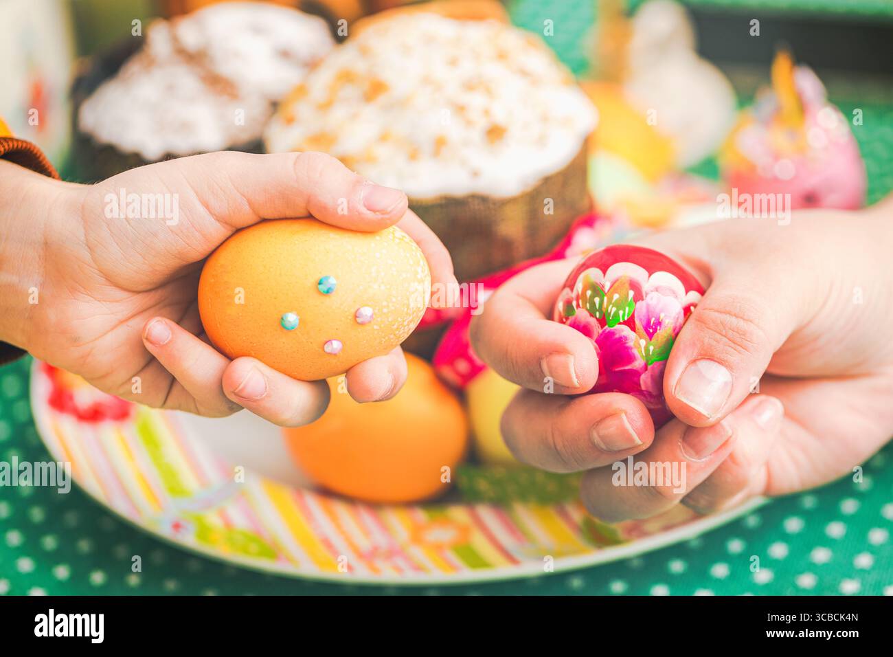 Tradizione pasquale di famiglia. Figlia e madre picchiano le uova di Pasqua contro Kulich o la torta pasquale Foto Stock
