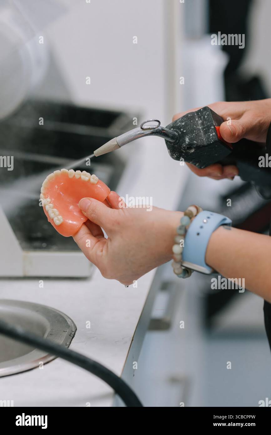 Pulizia protesi dentarie con spruzzatore d'acqua in laboratorio. Foto Stock