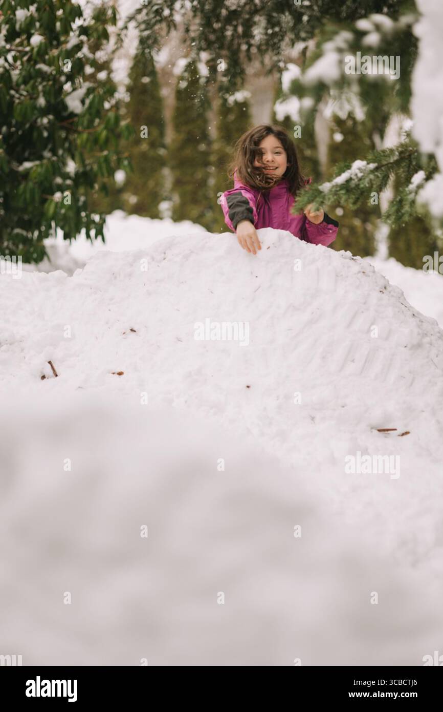 Bambino in giacca rosa che gioca in cima a un grande tumulo innevato all'aperto Foto Stock