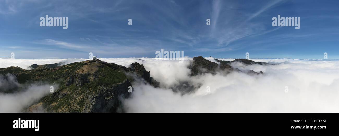 Vista aerea delle cime rocciose che penetrano attraverso un mare di nuvole, un osservatorio annidato in cima al punto più alto, Pico do Arieiro, Madeira, Portogallo. Foto Stock
