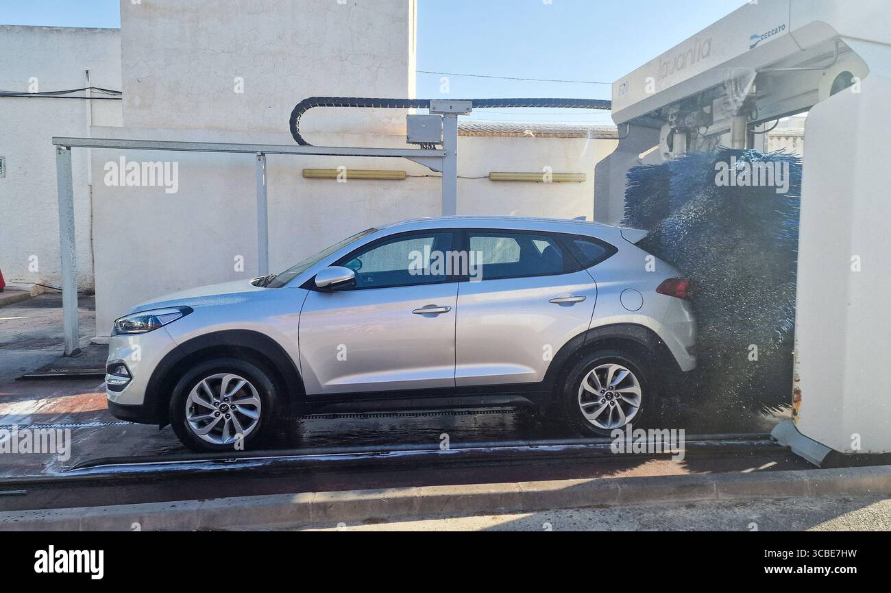 Il SUV Silver viene pulito in un autolavaggio automatizzato, con spazzole rotanti e getti d'acqua, evidenziando la manutenzione del veicolo e la tecnologia moderna Foto Stock