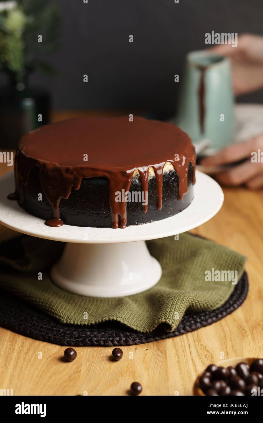 Affettare a mano una ricca cheesecake con una crosta scura, con strati cremosi di vaniglia e cioccolato, ricoperti di ganache al cioccolato lucido. Foto Stock