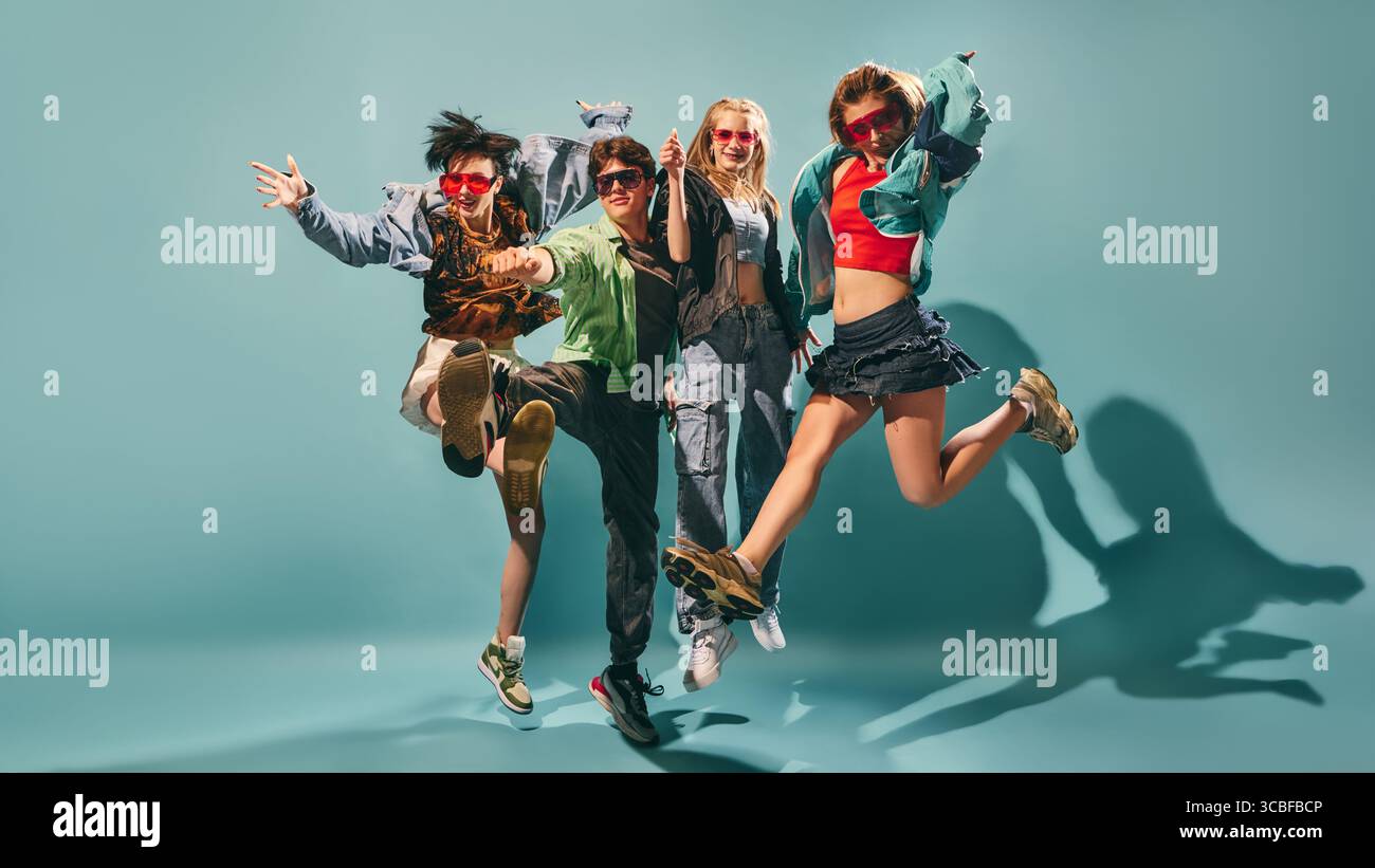 Gruppo energico di giovani che saltano in streetwear colorato sullo sfondo turchese dello studio Foto Stock