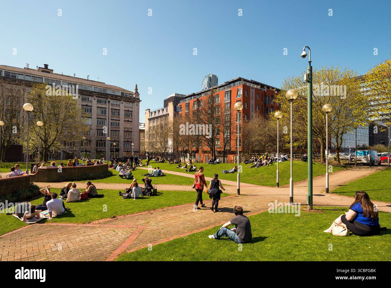 Persone che si rilassano e socializzano in un parco urbano soleggiato nel centro di Liverpool, circondato da un'architettura storica e moderna. Foto Stock