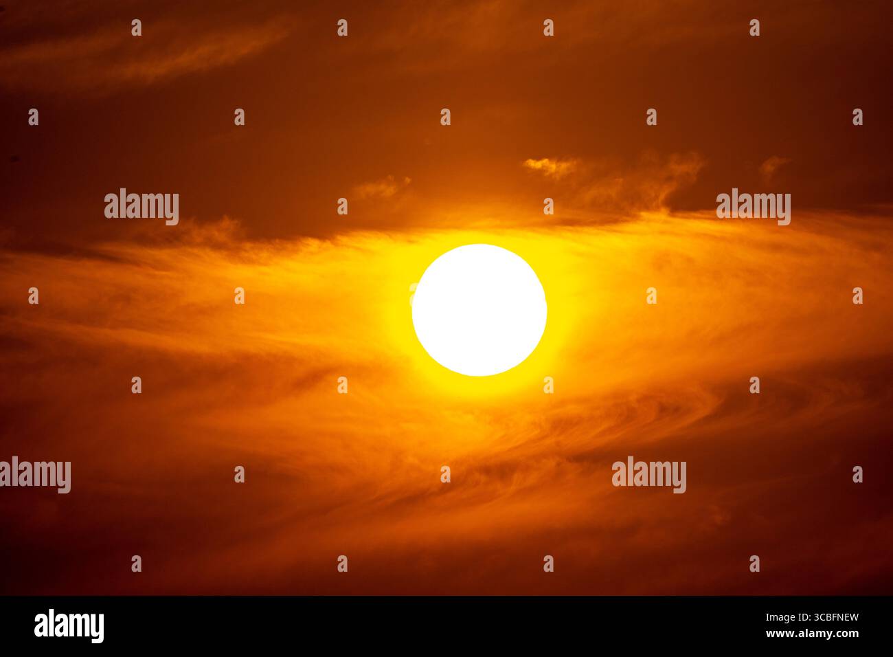 Un incredibile teleobiettivo in primo piano del sole che tramonta, che brilla di calore intenso in un bellissimo cielo arancione. Foto Stock