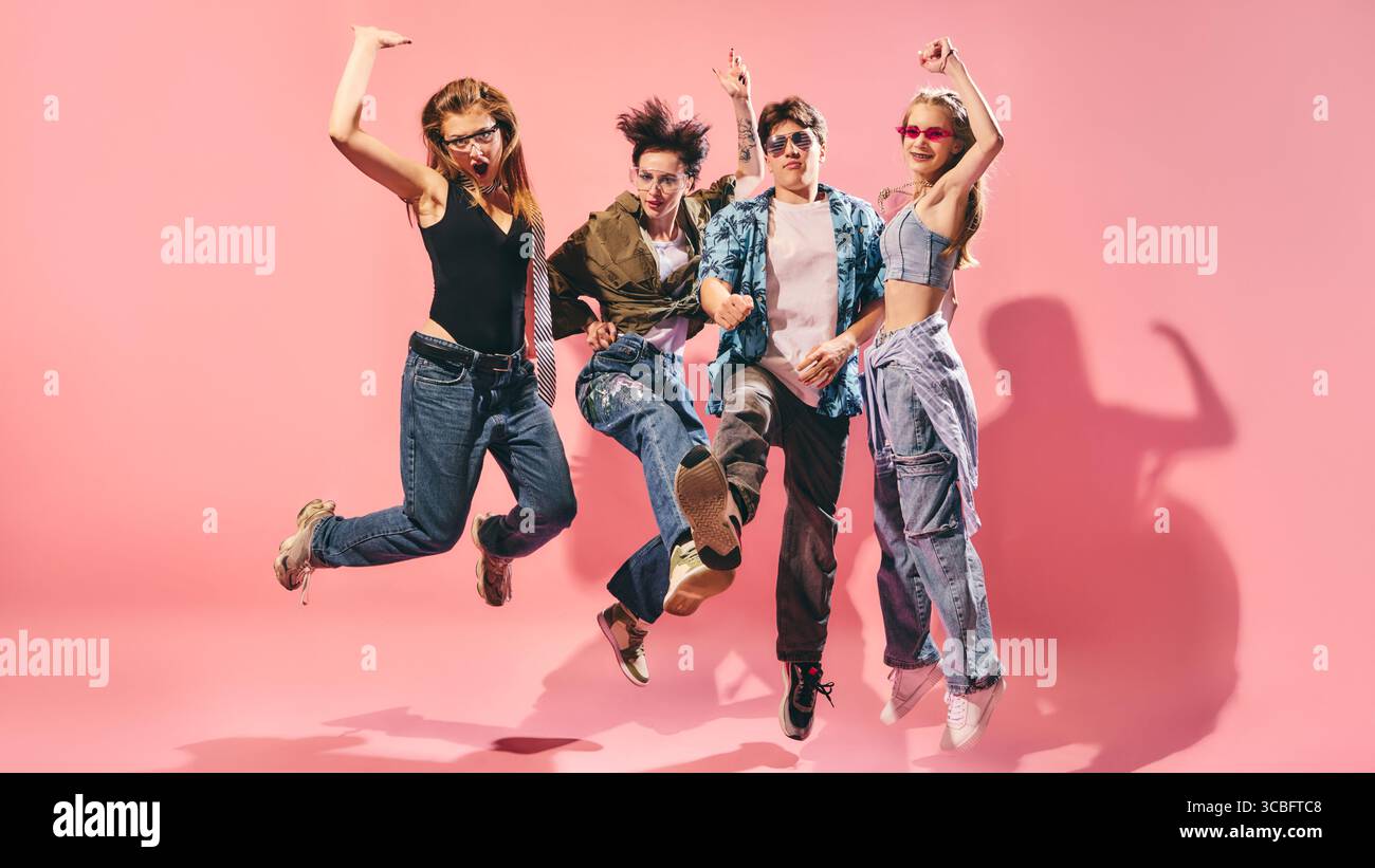 Energico gruppo giovanile che salta in streetwear elegante su sfondo rosa Foto Stock
