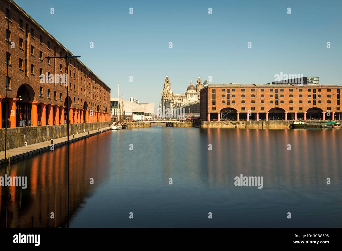 I magazzini Albert Dock con riflessi sull'acqua, si affacciano sulle iconiche tre Grazie di Liverpool. Foto Stock