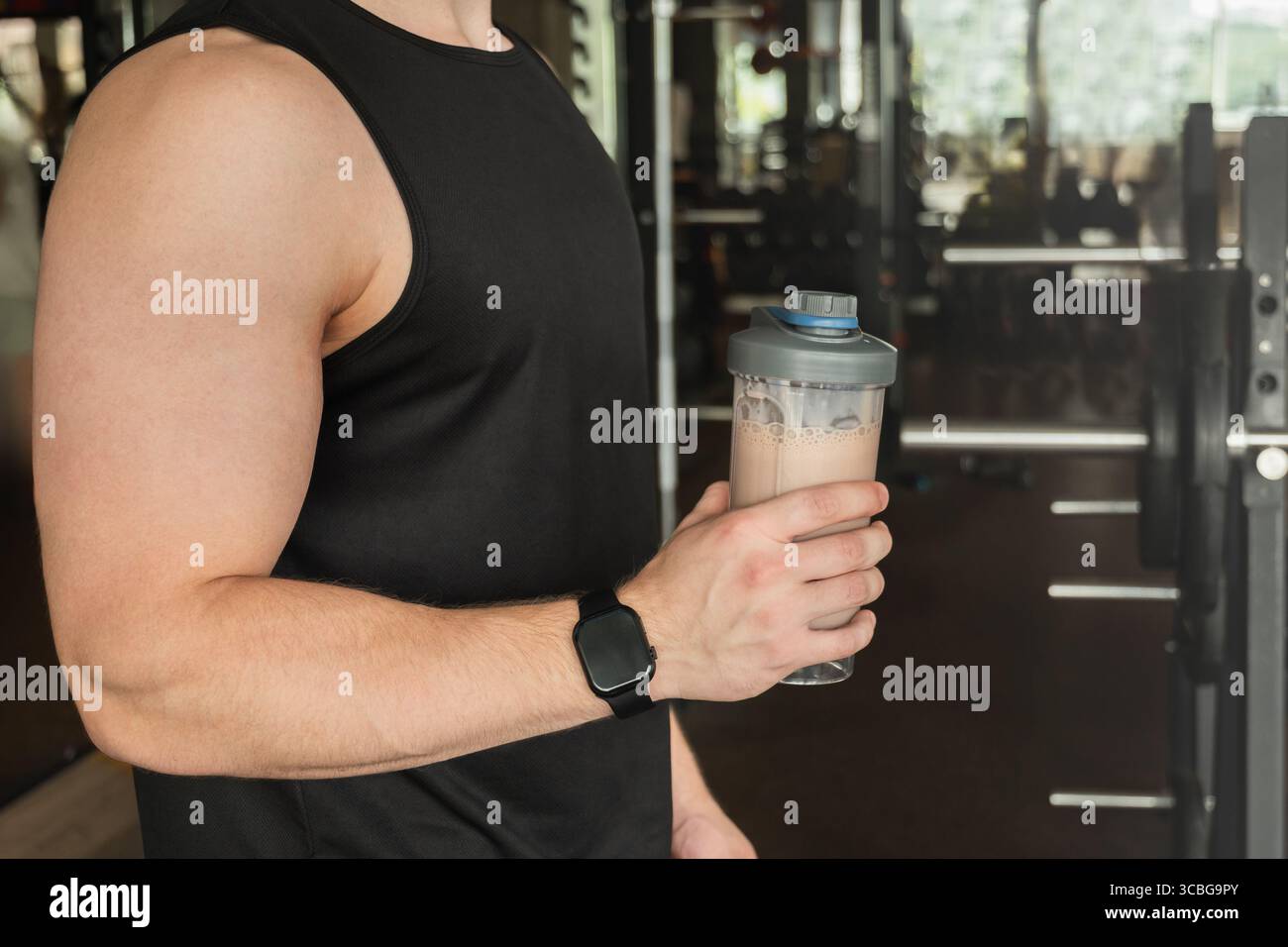 Fai una mano all'uomo sportivo con un frullato proteico mentre ti alleni in palestra o nel centro fitness. Assistenza sanitaria e allenamento. Vista laterale. Foto Stock