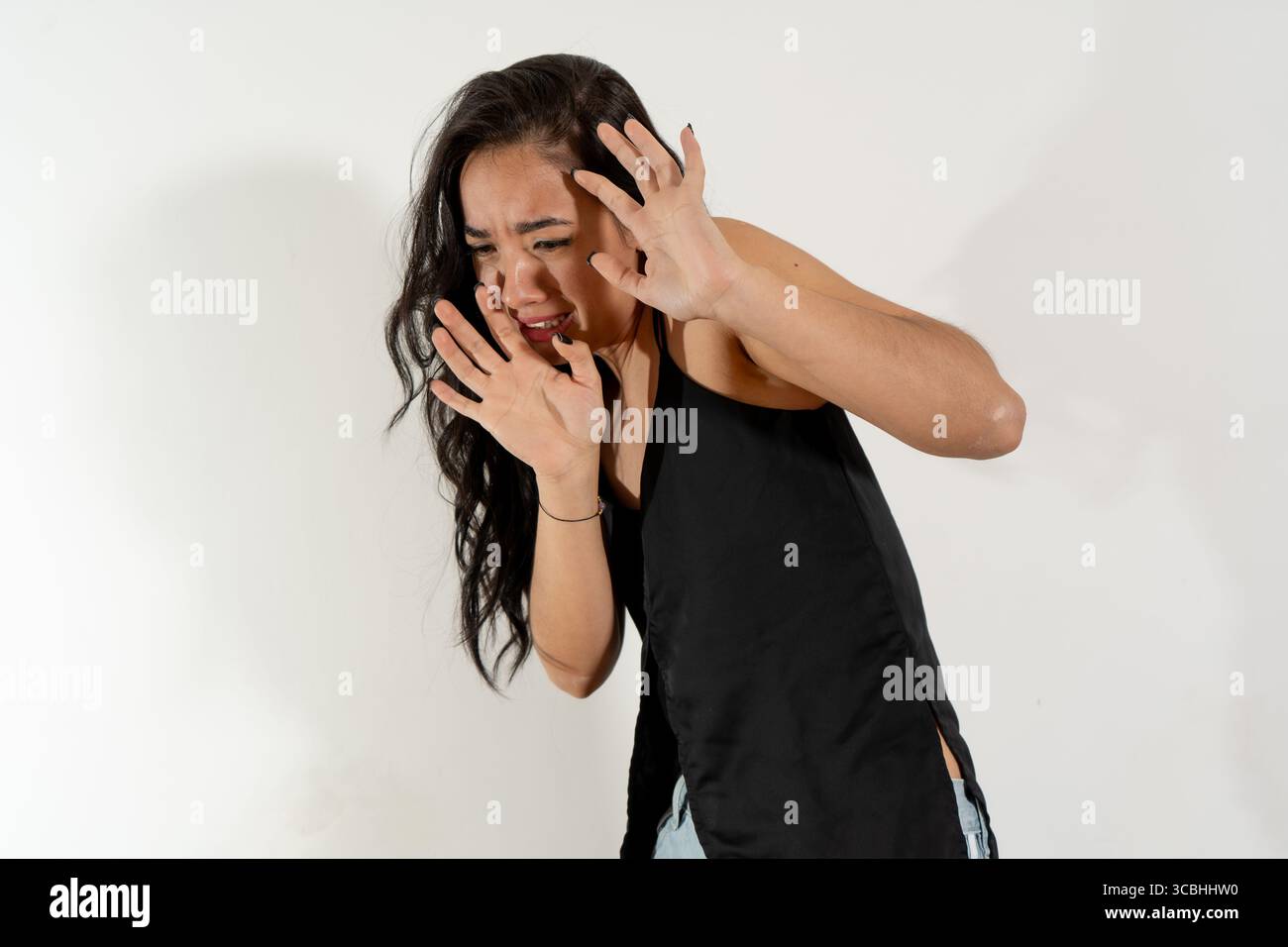 Foto in studio di una giovane donna che mostra paura e ansia, alzando le mani in un gesto difensivo Foto Stock