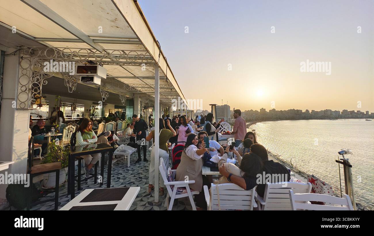 Turisti e gente del posto si rilassano e scattano selfie in un ristorante sulla terrazza ad Alessandria, in Egitto, durante un bellissimo tramonto Foto Stock