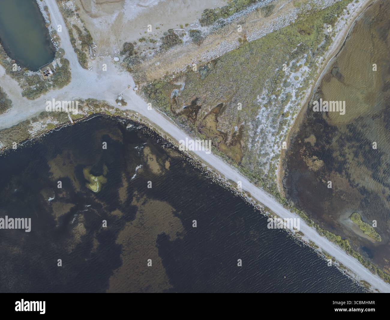 Veduta aerea del netto contrasto tra le acque scure e la terra pallida e strutturata, divisa da sottili sentieri, Gruissan, Occitanie, Francia. Foto Stock