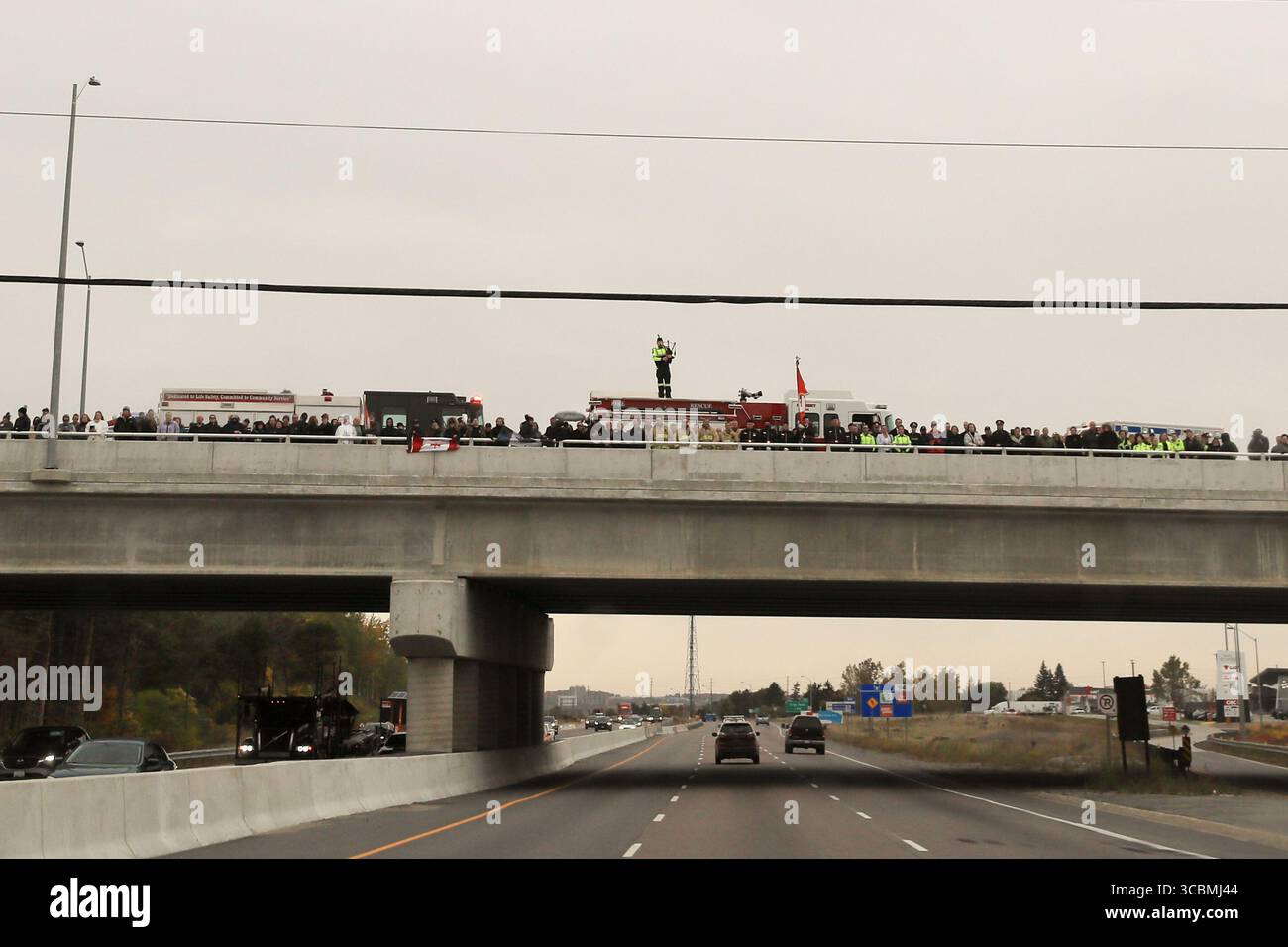 14 ottobre 2022, Innisfil, Ontario, Canada: Un giocatore solitario di cornamuse visto con servizi di emergenza e pubblico che tiene bandiere canadesi sul cavalcavia Big Bay Point Highway 400 preparandosi a salutare la processione di due agenti della polizia di South Simcoe uccisi che hanno risposto a una chiamata di disturbo domestico ad Alcona (Innisfil), Ontario - una piccola città nel centro-sud dell'Ontario, a circa un'ora a nord di Toronto. (Immagine di credito: © Christopher Drost/SHIFT digital tramite ZUMA Press Wire) Foto Stock