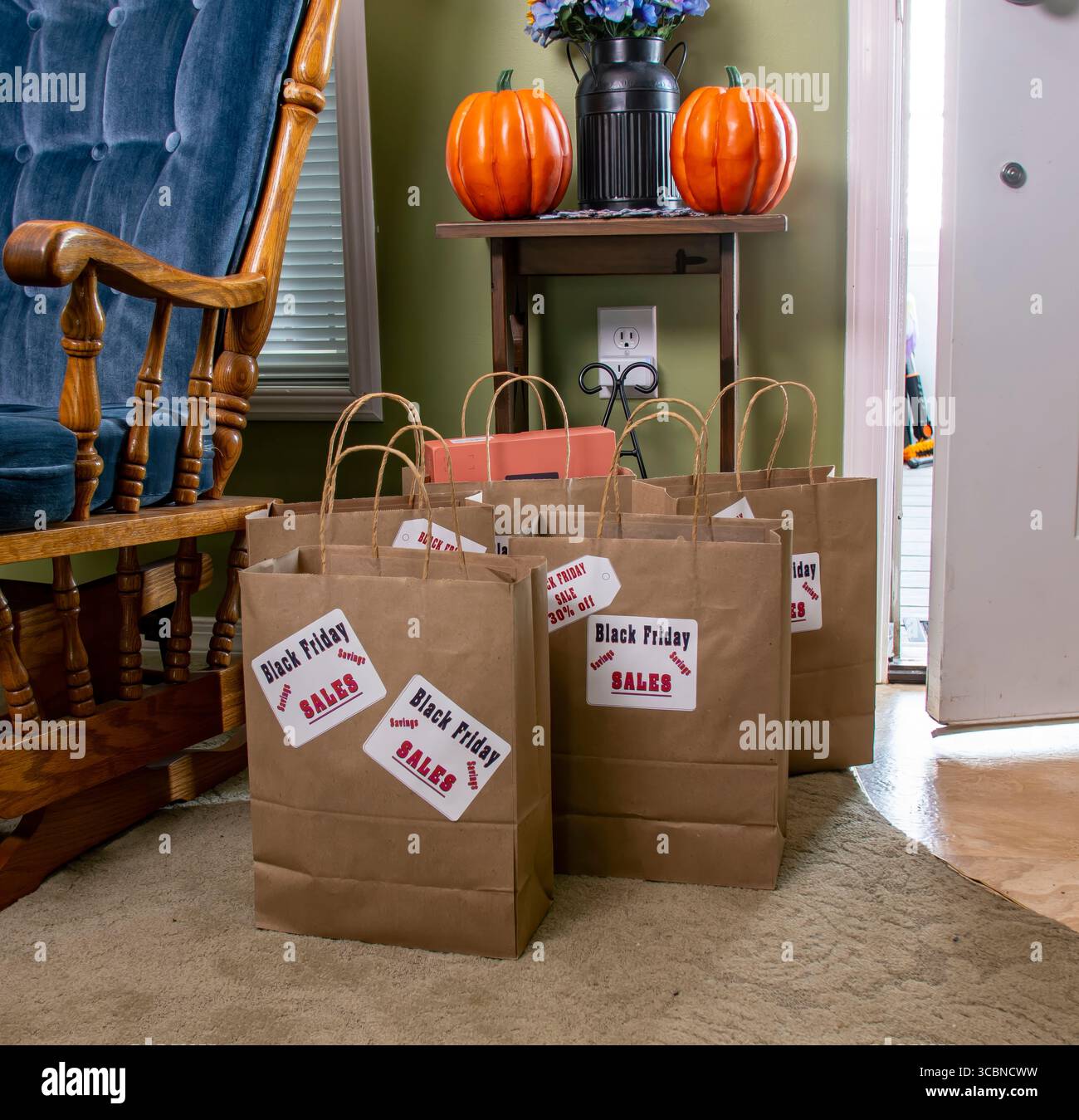 Le borse con cartellino di vendita per il Black Friday si trovano sul pavimento accanto a una comoda sedia a dondolo. L'ambientazione presenta decorazioni autunnali che indicano la stagione A. Foto Stock