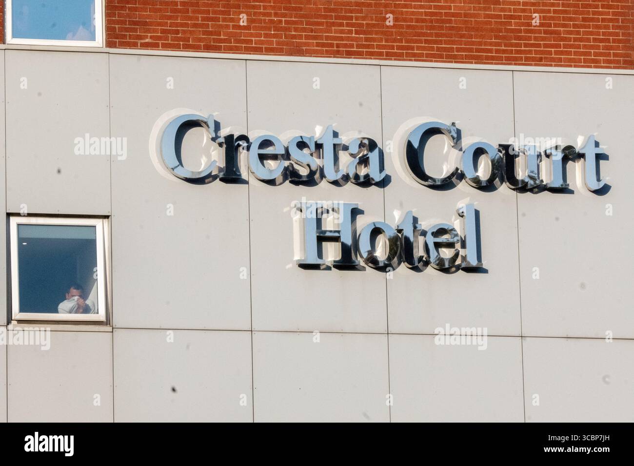 Manchester, Regno Unito. 8 agosto 2025. I rifugiati guardano la protesta dalla finestra dell'hotel. Protesta e contro protesta al Cresta Court Hotel, Altrincham, Manchester Regno Unito. I manifestanti anti anti-migranti discutono con la polizia. I manifestanti preoccupati per l'uso dell'hotel per ospitare i richiedenti asilo riuniti nel tardo pomeriggio. I manifestanti includevano il gruppo delle donne i “manifestanti rosa”. Una contro protesta di “Stand Up to Racism” si è riunita anche in hotel. La polizia separò i due gruppi e una barriera temporanea era in atto nella riserva centrale. Altrincham, Manchester. Crediti: GaryRobertsphotography/Alamy Live News Foto Stock