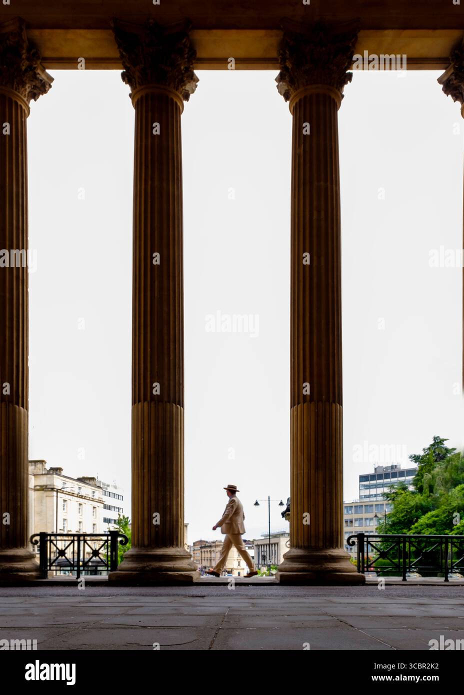 Un uomo con tuta e cappello cammina tra grandi colonne. Foto Stock