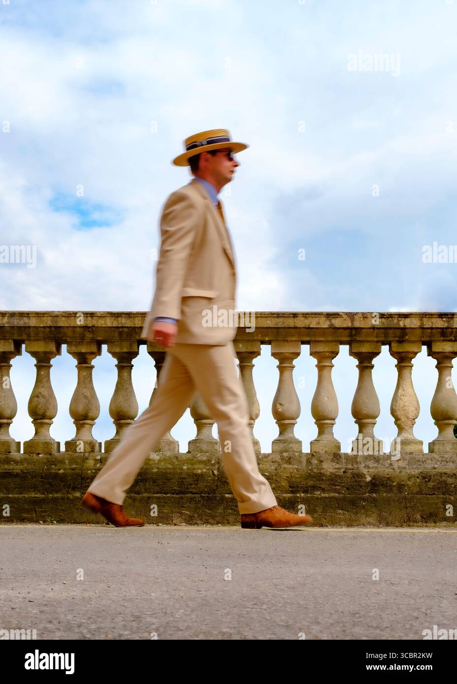 Un uomo con un abito abbronzato e un cappello di paglia cammina lungo una balaustra di pietra. Foto Stock