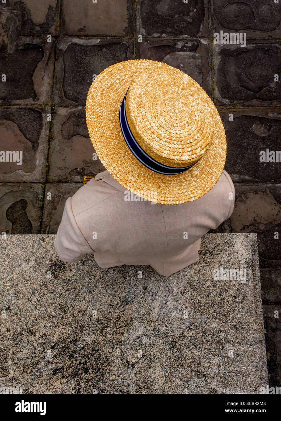 Una persona che indossa un cappello di paglia e una giacca di colore chiaro viene vista dall'alto, in piedi su una superficie di pietra. Foto Stock