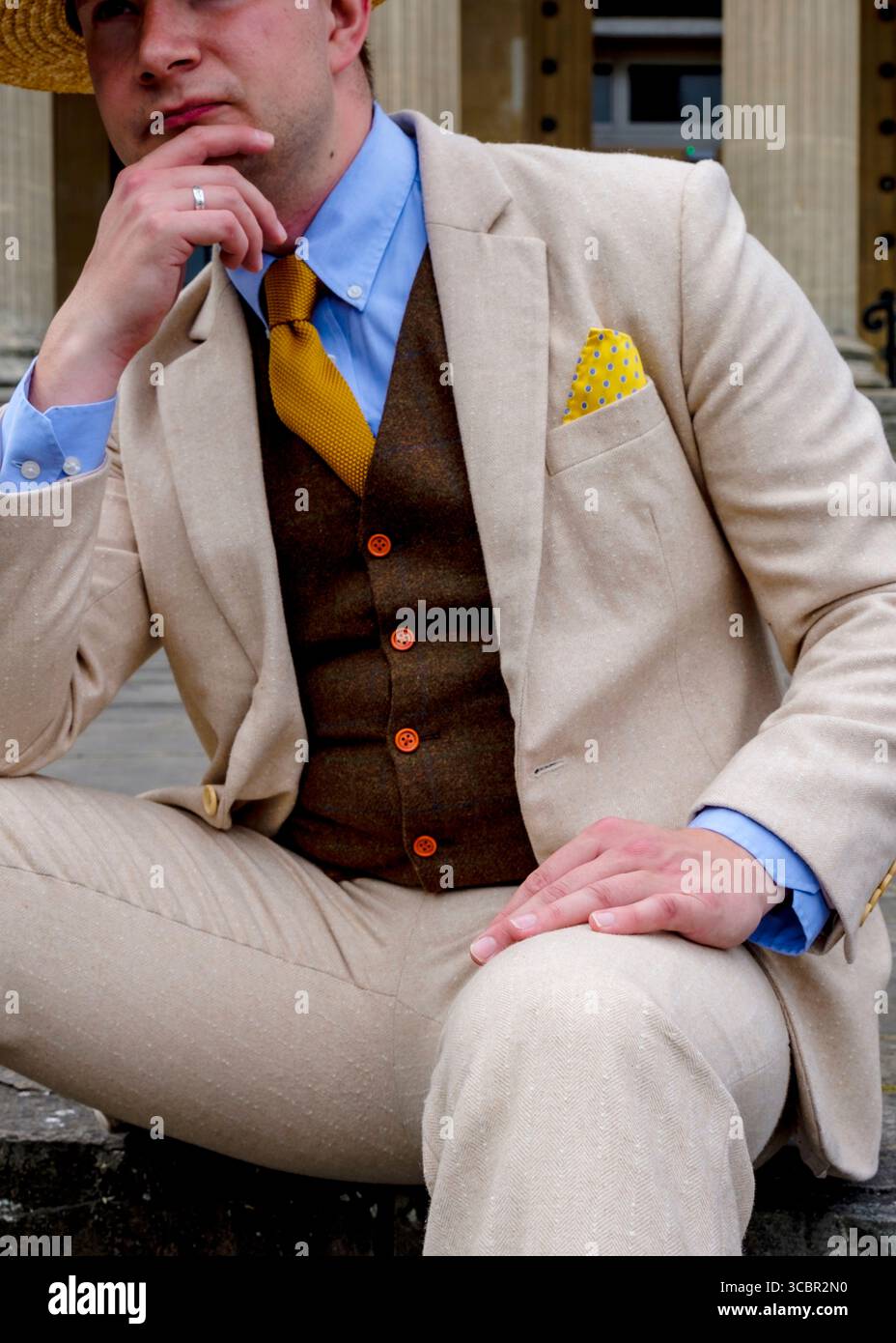 Un uomo con un abito elegante, completo di cappello di paglia, è seduto e tocca con cura il mento. Foto Stock