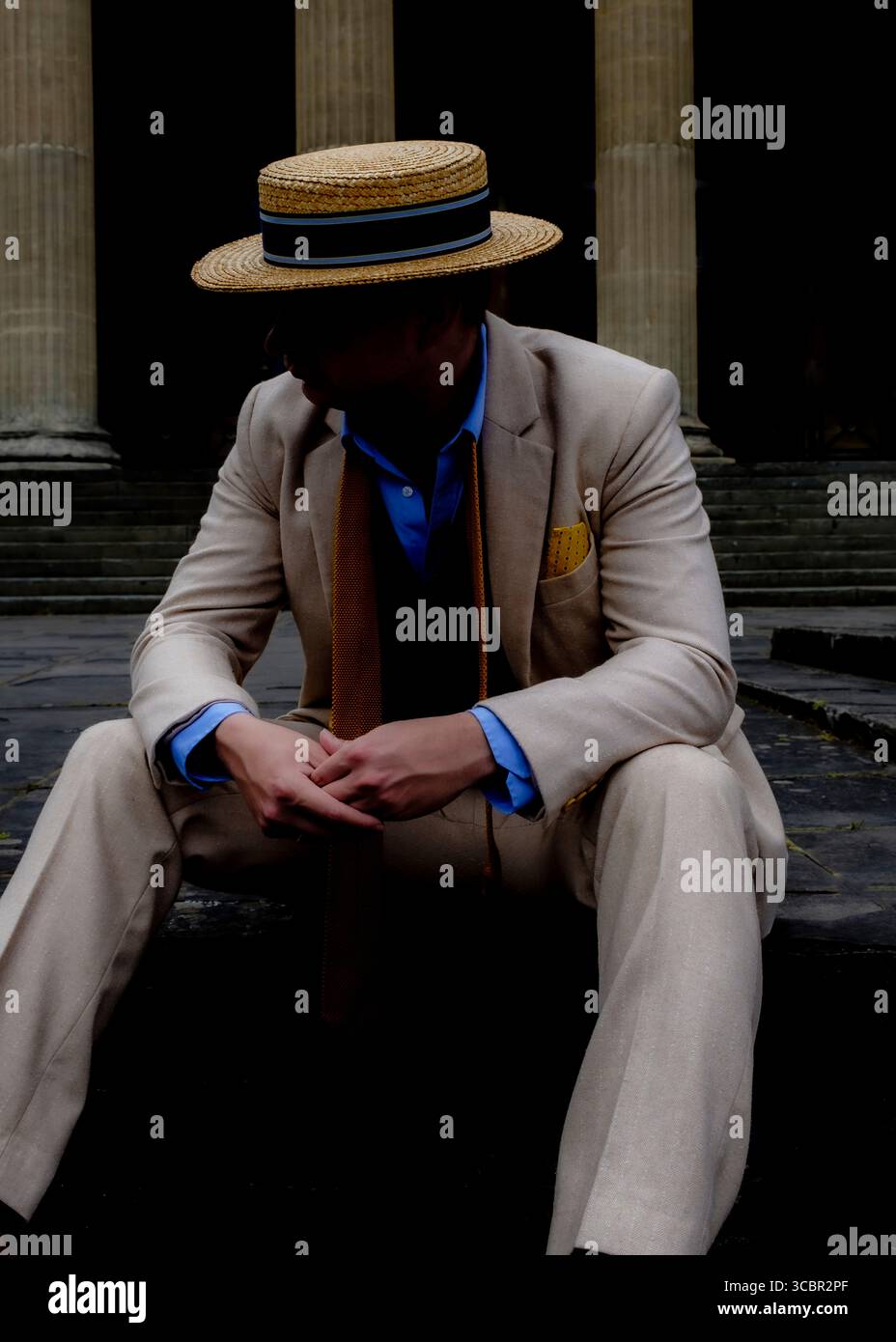 Un uomo con un cappello di paglia e una tuta si siede sui gradini di fronte a grandi colonne. Foto Stock