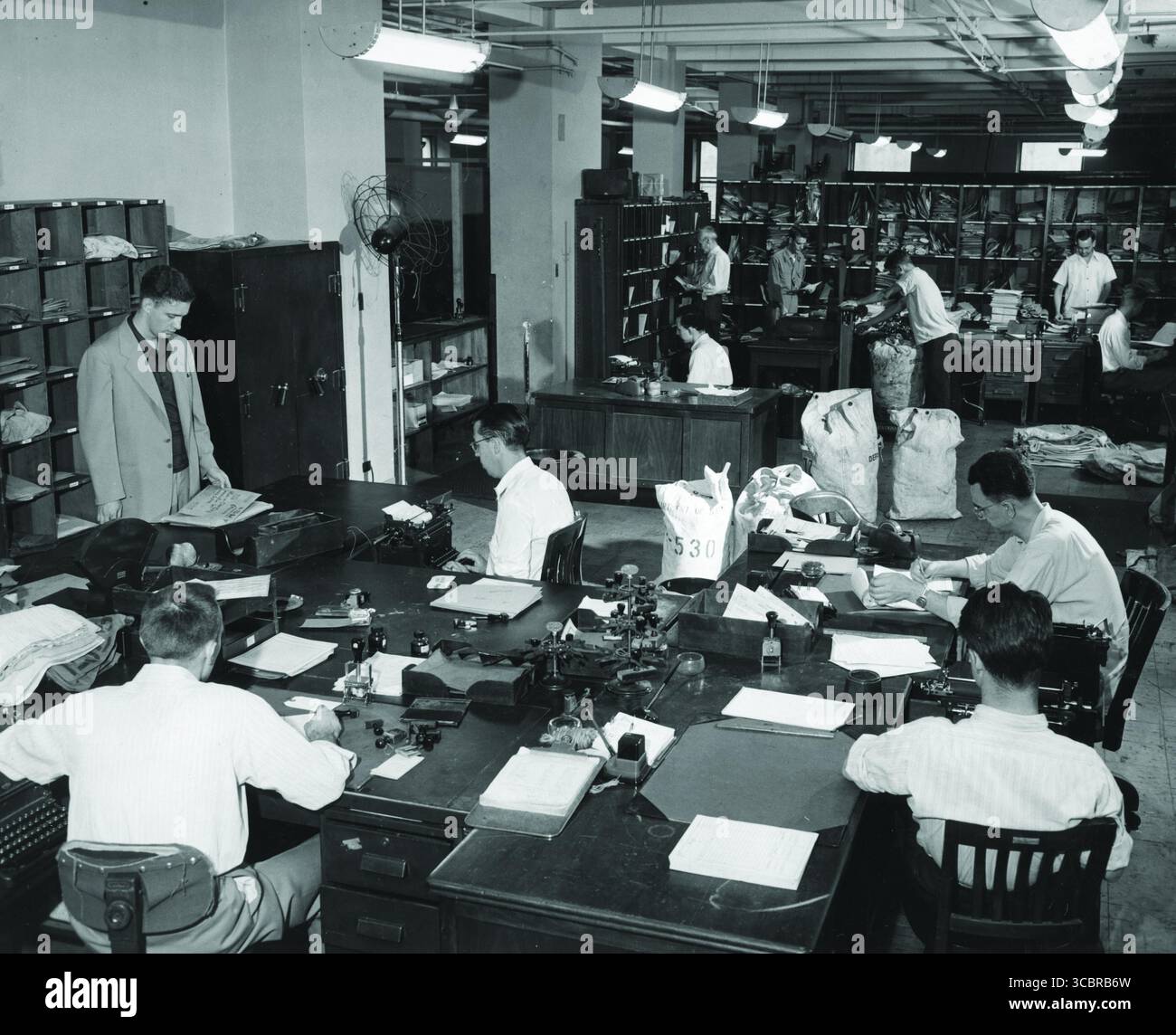 Foto della mail Room insieme ai corrieri diplomatici, tra cui l'agente speciale Roy Feltin, Un corriere diplomatico (a sinistra) attende nella stanza della posta del Dipartimento di Stato nel 1948, mentre i contenuti della busta diplomatica vengono ordinati e registrati. Dopo la seconda guerra mondiale, i corrieri sostituirono gli agenti Despatch come principali vettori del dipartimento di documenti importanti. Il sistema di corriere ha portato, in parte, a un notevole sviluppo del trasporto aereo. Fonte: Dipartimento di Stato. Foto Stock