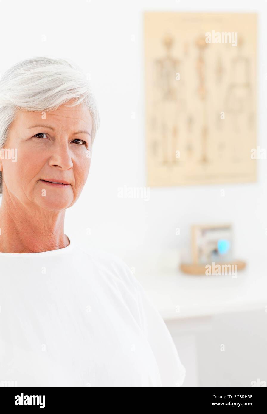 Donna anziana seduta in clinica con cartella anatomica, scrivania bianca e oggetto incorniciato, spazio di copia Foto Stock