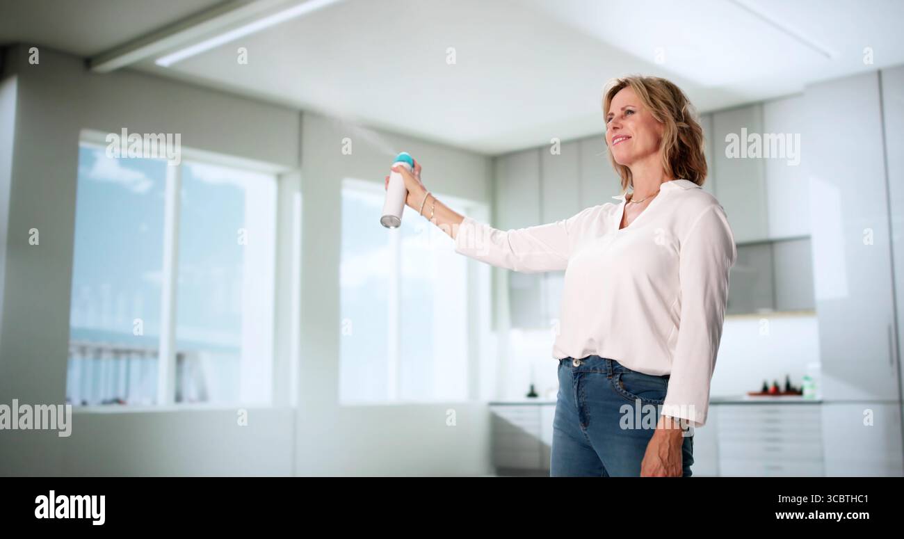 La donna spruzza aria fresca per deodorizzare il suo salotto. La donna anziana usa Air Freshener sul suo tappeto Foto Stock