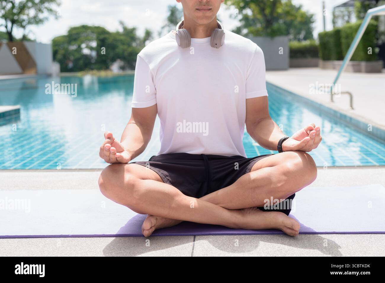 Uomo in forma seduto in posa meditativa a bordo piscina. Momento di calma e tranquillità che riflette yoga, consapevolezza, concentrazione spirituale e sano stile di vita estivo Foto Stock