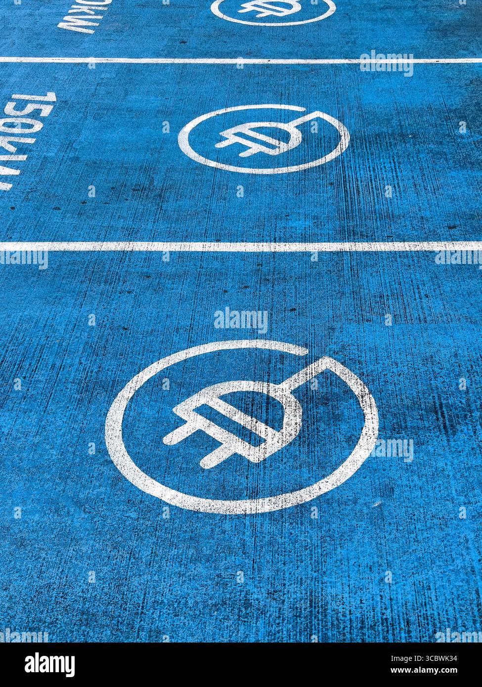 Vista dall'alto del piazzale blu della stazione di ricarica per auto elettriche con grafica a spina e segnaletica da 150 kW sul piazzale del garage Foto Stock