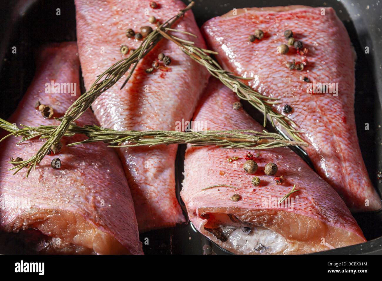 Il pesce crudo si trova in un primo piano di una teglia di ghisa Foto Stock