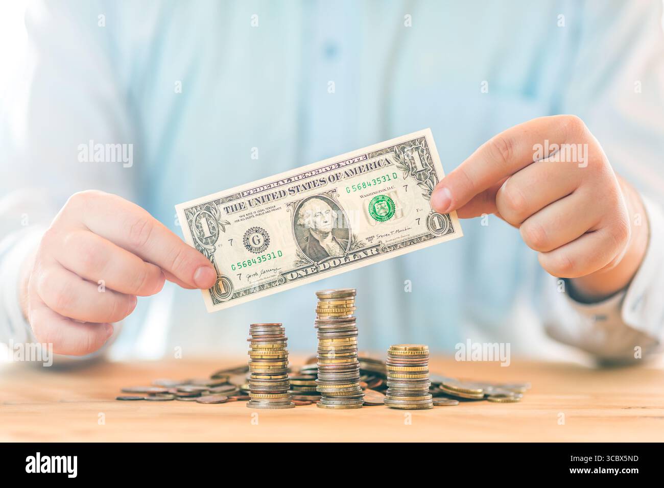 Risparmio di denaro. Concetto di contabilità, business, budget e finanza. Mani maschili che tengono una banconota da un dollaro sopra le pile di monete Foto Stock