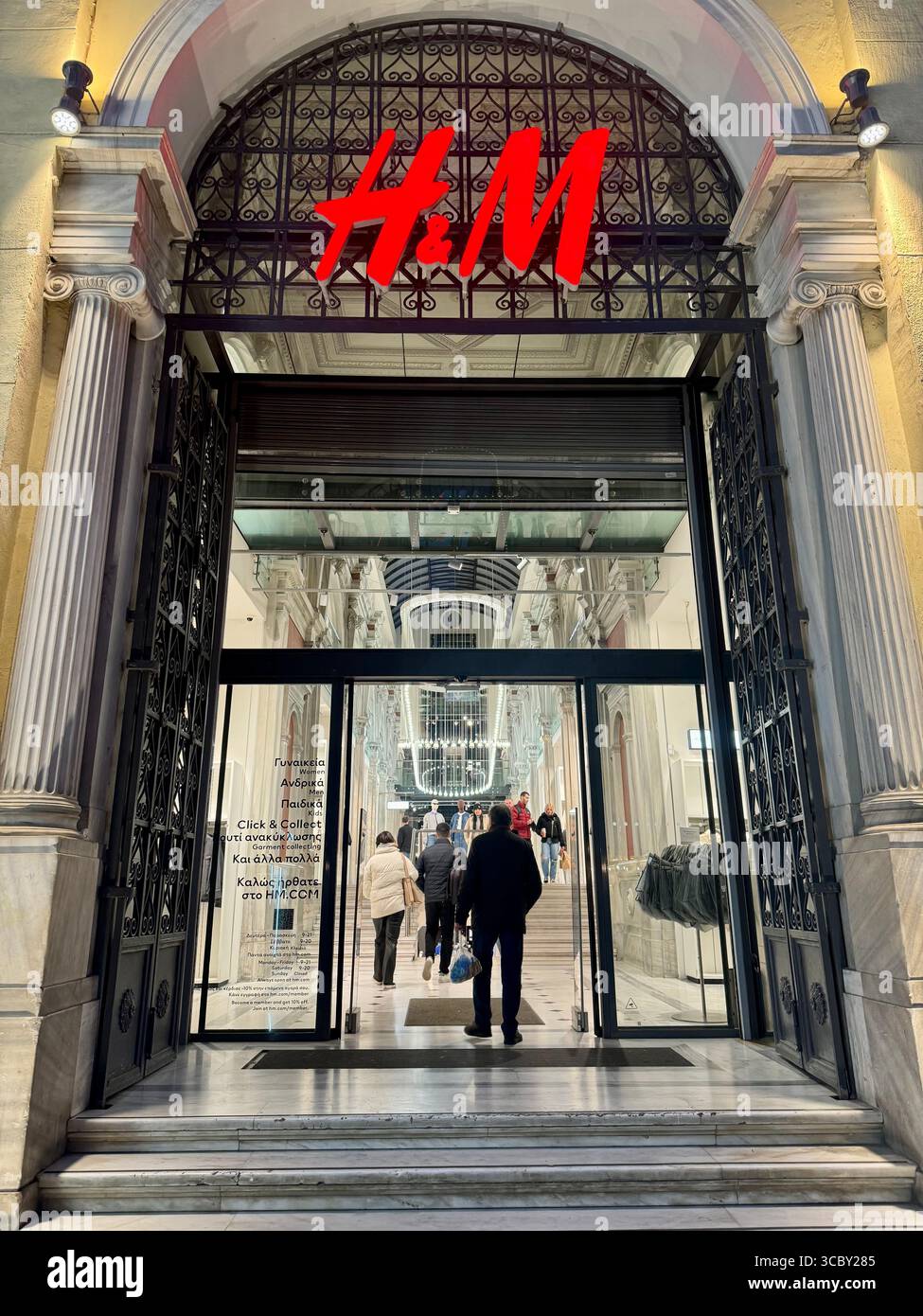 Elegante ingresso al negozio H&M di Atene, Grecia, di notte con persone che entrano. - Immagine stock catturata con smartphone