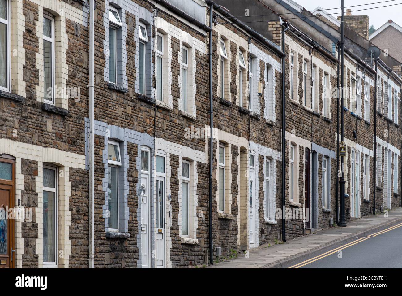 Fila di case a schiera nella città di Caerphilly (Caerffili), Galles del Sud, Regno Unito, pareti rocciose con coloratissimi bendaggi in mattoni Foto Stock
