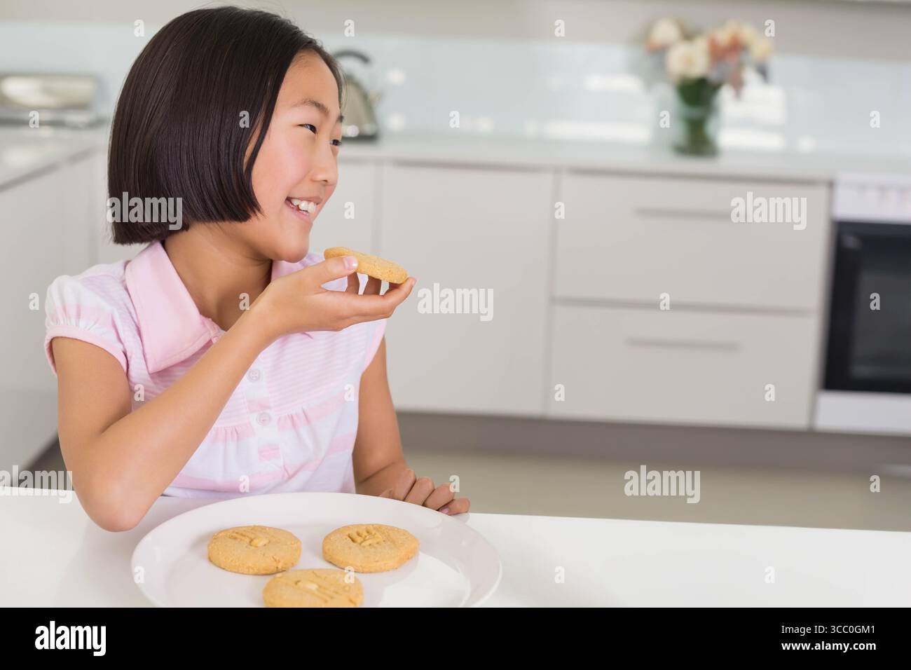 I biscotti rotondi poggiano su un tavolo bianco, con bollitore d'acciaio e vaso di fiori pallidi Foto Stock