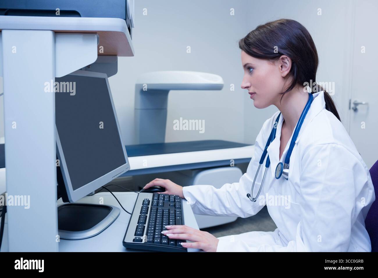 Apparecchiatura di imaging medicale in piedi accanto al monitor da tavolo e alla tastiera in una sala clinica dai colori chiari Foto Stock
