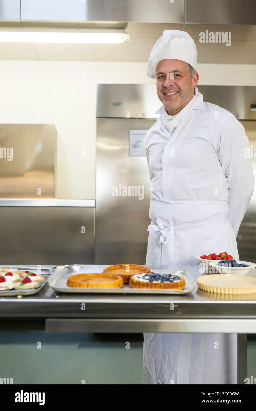 Pasticcere maschile in piedi dietro un tavolo di preparazione in acciaio che prepara crostate di frutta in cucina, spazio per copiare Foto Stock