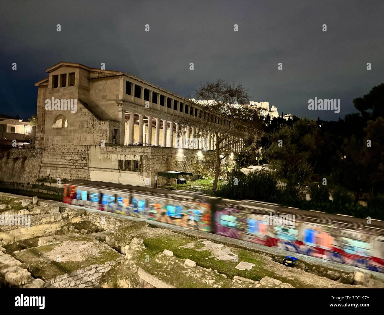 Le rovine della basilica romana con la metropolitana ricoperta di graffiti, l'antica Agorà e l'Acropoli sullo sfondo, Atene, Grecia di notte. Foto Stock