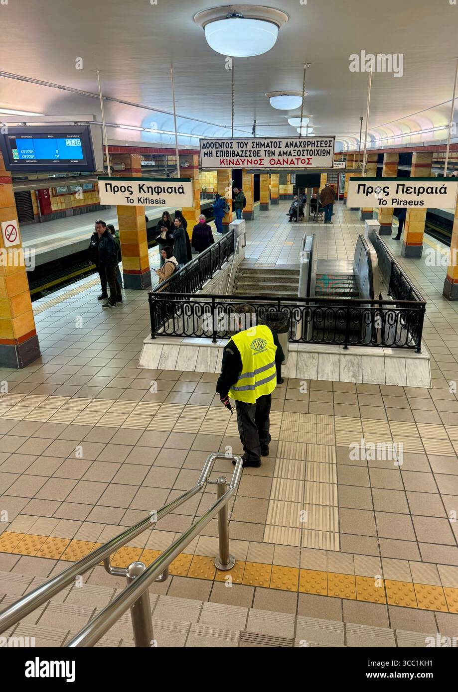 Personale di sicurezza che pattuglia una stazione metropolitana interna di Atene con pendolari e scale mobili. Foto Stock