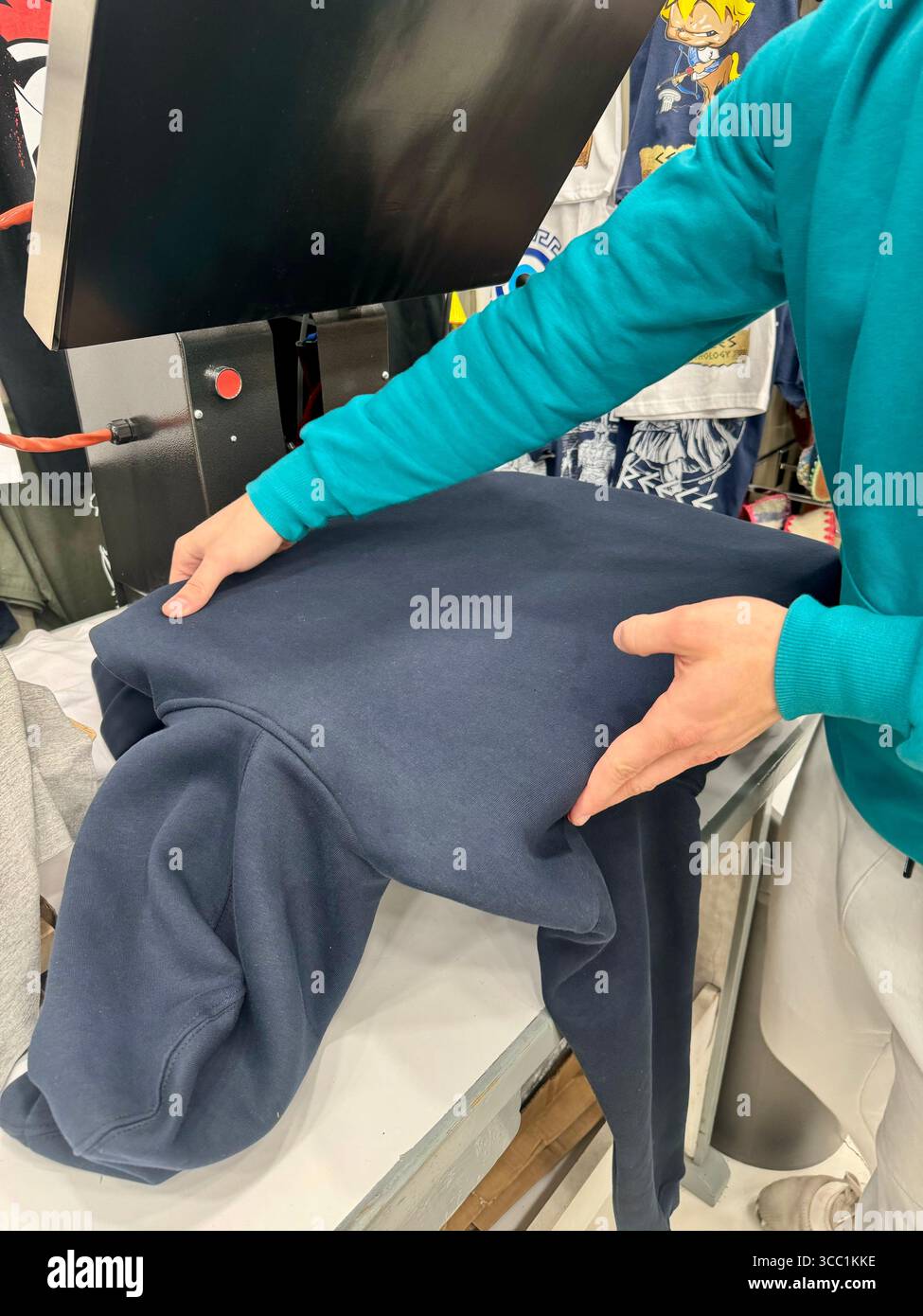 Un lavoratore si sta preparando a stampare su una felpa utilizzando una pressa da stampa in un'officina tessile. - Immagine stock catturata con smartphone