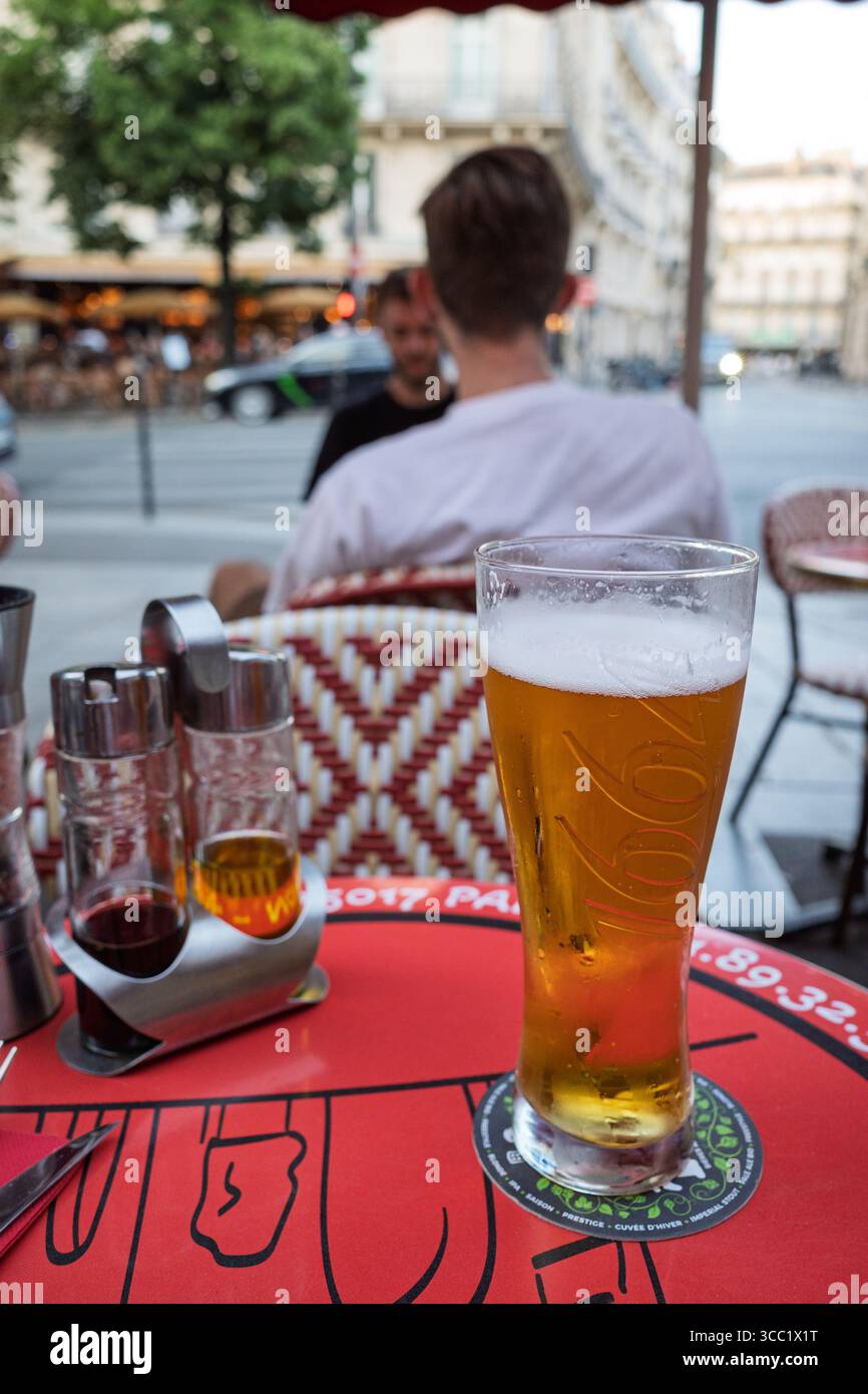 Un bicchiere di birra e condimenti su un tavolo da caffè rosso a Parigi con una persona sullo sfondo. Foto Stock Un bicchiere di birra e condimenti su un tavolo da caffè rosso a Parigi con una persona sullo sfondo. Foto Stock