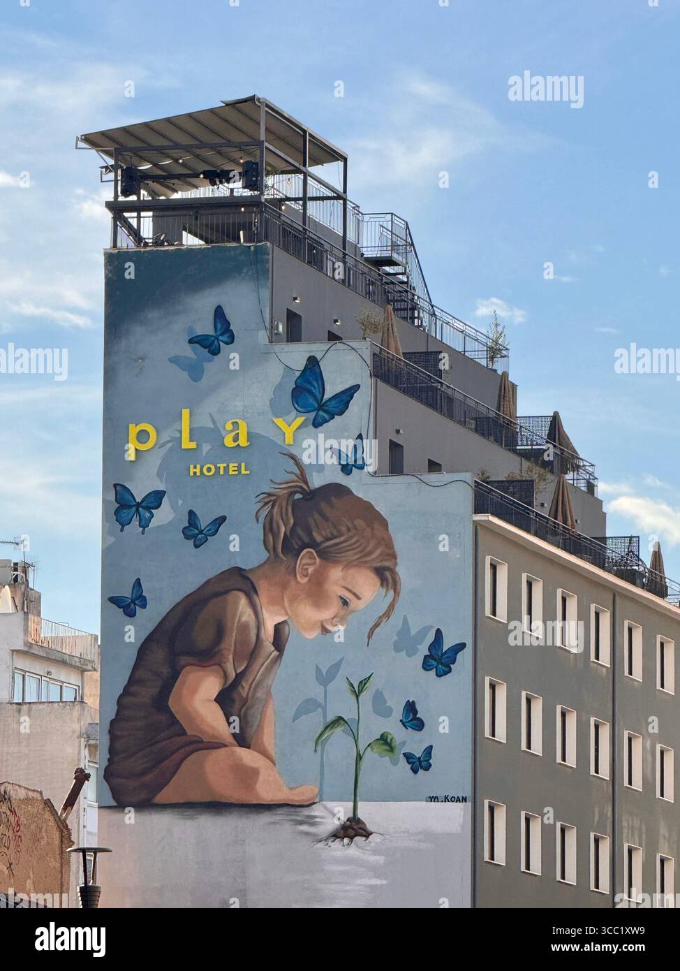 Murale di Street art in un edificio di Atene che raffigura un bambino che interagisce con la natura, circondato da farfalle e dalla parola "giocare". - Immagine stock catturata con smartphone