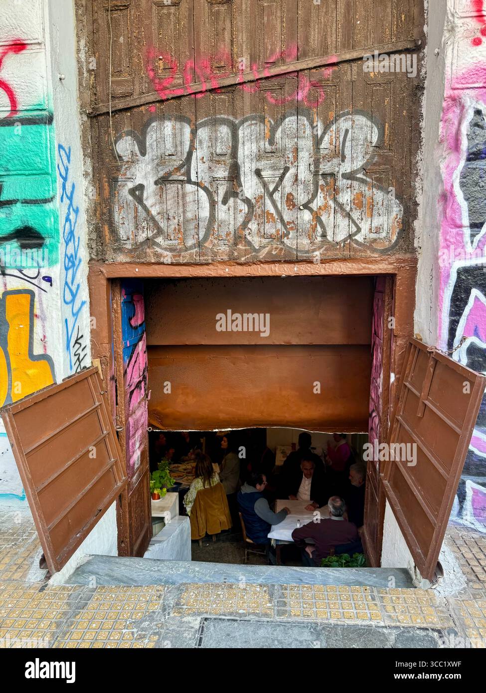 Ingresso a una tradizionale taverna greca, che mostra una porta rustica con la gente che cena all'interno. - Immagine stock catturata con smartphone