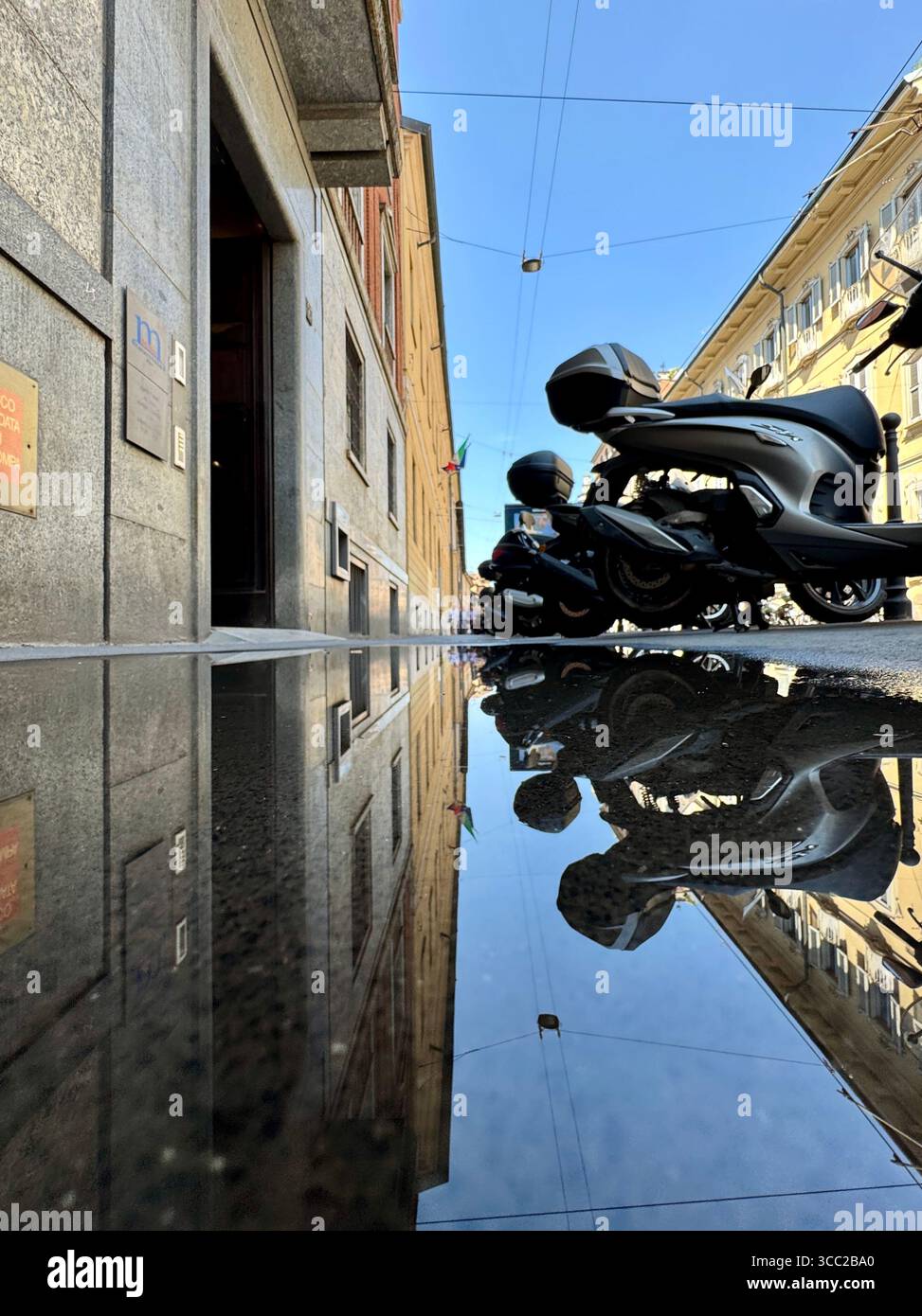 Gli scooter parcheggiati in strada a Milano, Italia, si riflettono in pozzanghere dopo la pioggia, nel paesaggio urbano. Foto Stock