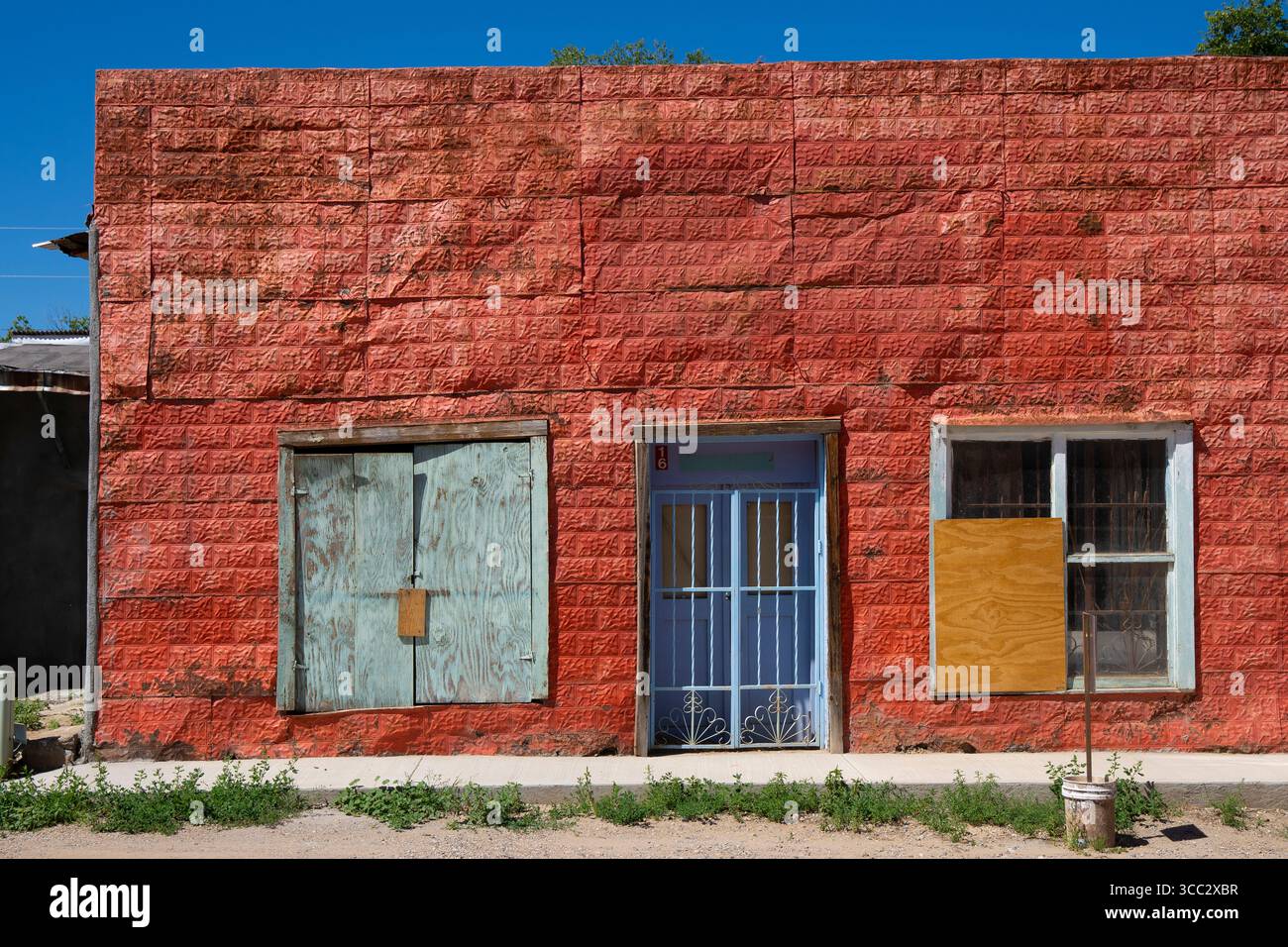 Vecchio esterno in metallo pressato di un edificio a Rancho de Taos, New Mexico. Colore rosso intenso sul metallo pressato e su sportello e finestra di colore blu e acqua Foto Stock