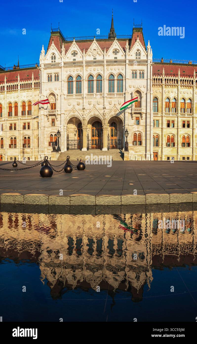 Edificio del Parlamento ungherese a Budapest, riflesso nell'acqua, splendida architettura neogotica con bandiere Foto Stock