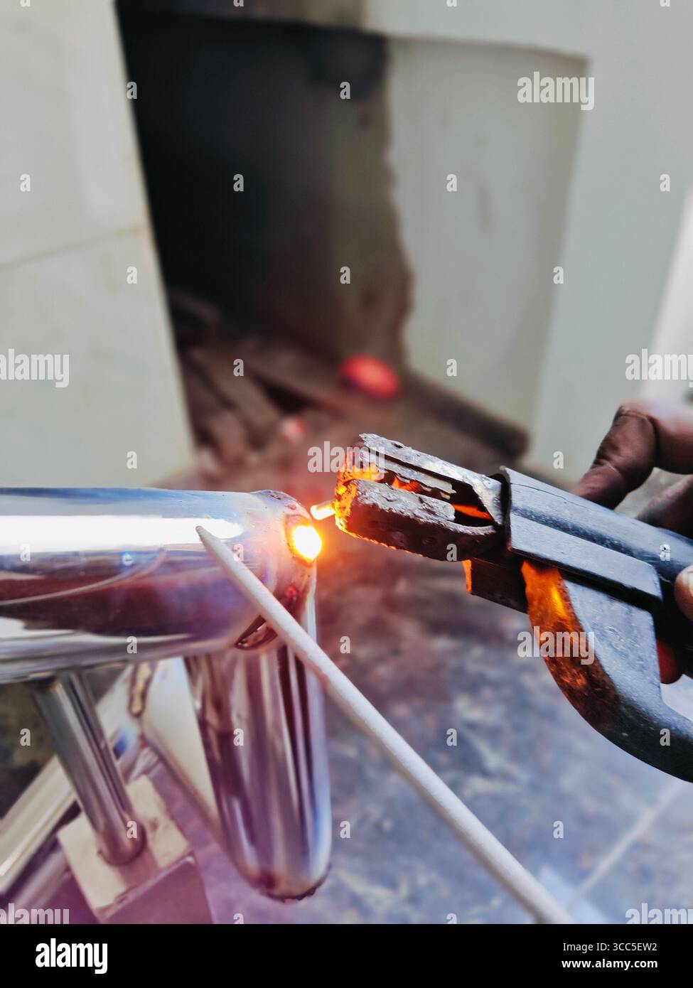 Un saldatore unisce con competenza due tubi metallici lucidati utilizzando una bacchetta di saldatura e un morsetto - Immagine stock catturata con smartphone
