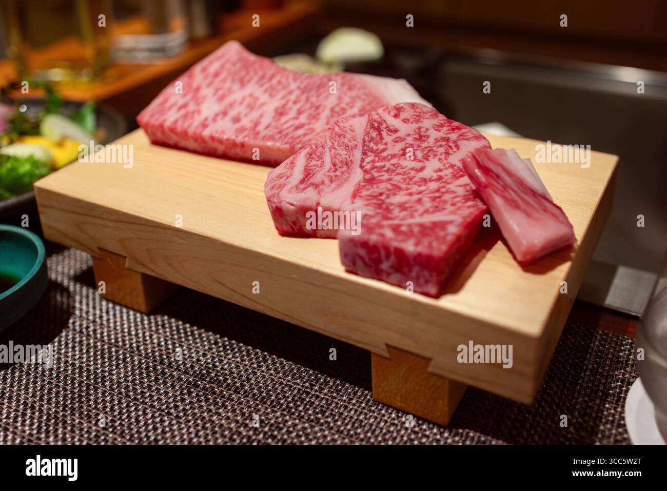 Manzo Kobe crudo di prima qualità servito su un tradizionale vassoio di legno con marmellate visibili, parte di un pasto teppanyaki in un raffinato spazio da pranzo giapponese Foto Stock