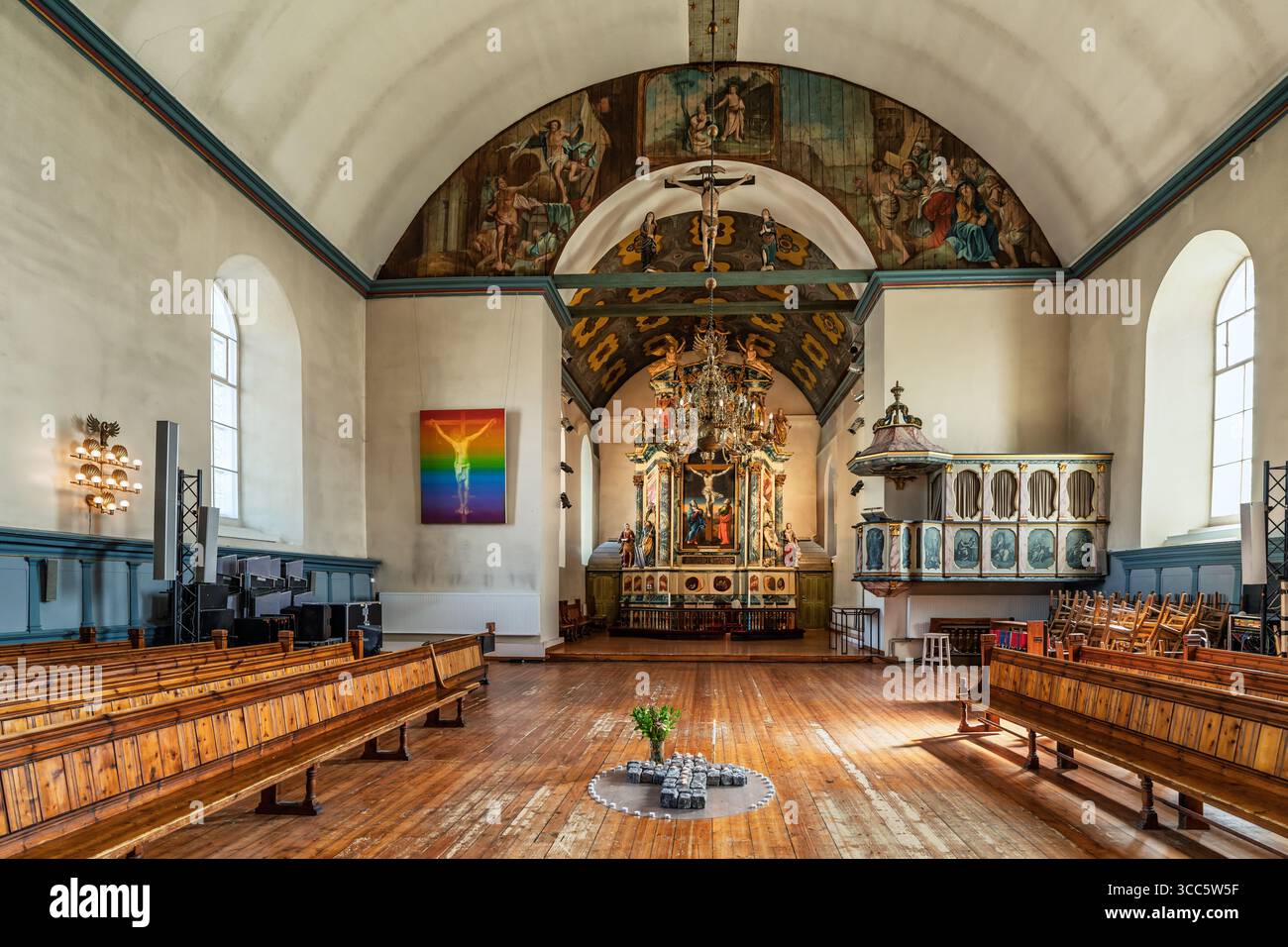 L'interno di una chiesa storica presenta un colorato altare e tradizionali pali di legno, completato da vibranti opere d'arte e intricati elementi decorativi Foto Stock