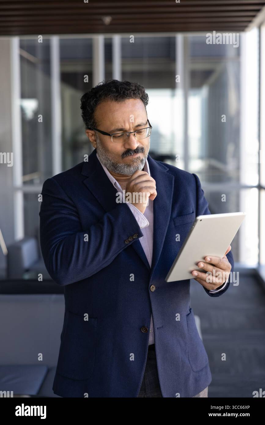 L'uomo anziano CEO indiano che legge o guarda contenuti online Foto Stock