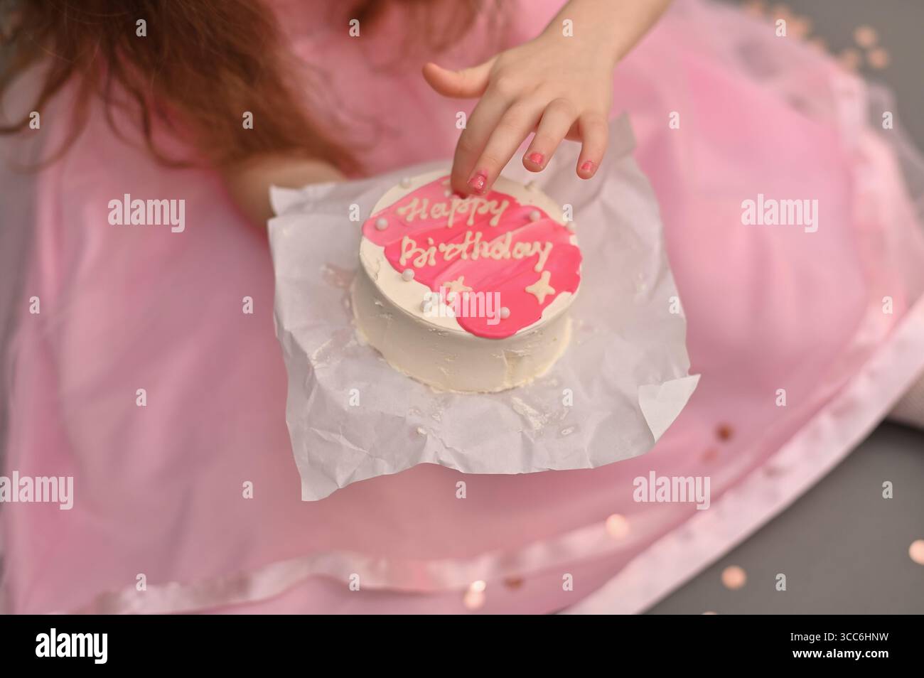 Primo piano di biscotti rosa a mano con buon compleanno scritto in glassa. la ragazza tiene in mano una torta decorata, sottolineando il tema del compleanno e. Foto Stock